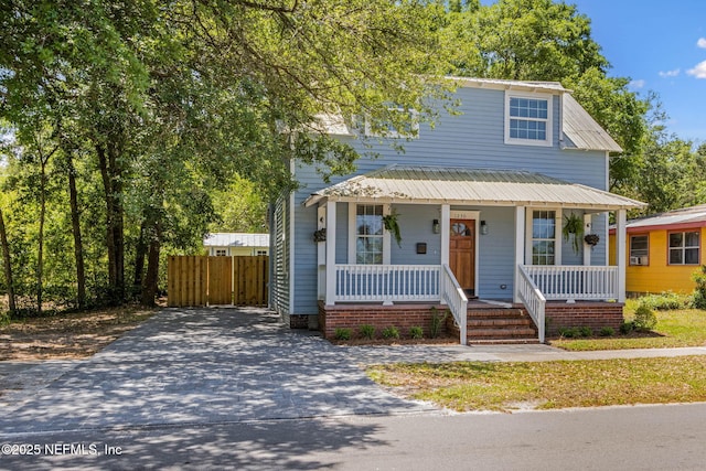 view of front of property featuring fence, concrete driveway, a porch, and metal roof