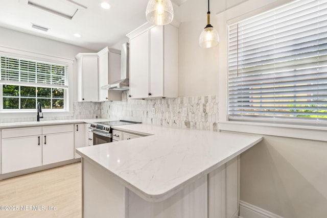 kitchen with decorative backsplash, a peninsula, wall chimney exhaust hood, a sink, and stainless steel range with electric cooktop