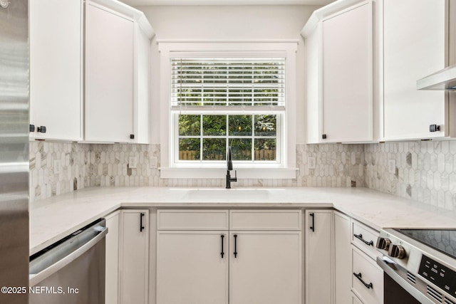 kitchen featuring tasteful backsplash, light stone countertops, a sink, stainless steel appliances, and white cabinetry