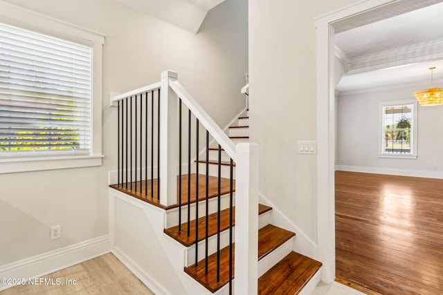 stairway with baseboards, an inviting chandelier, ornamental molding, and wood finished floors