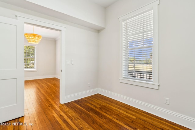 empty room with an inviting chandelier, baseboards, and hardwood / wood-style flooring