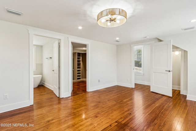 unfurnished bedroom with visible vents, a chandelier, a spacious closet, and hardwood / wood-style flooring