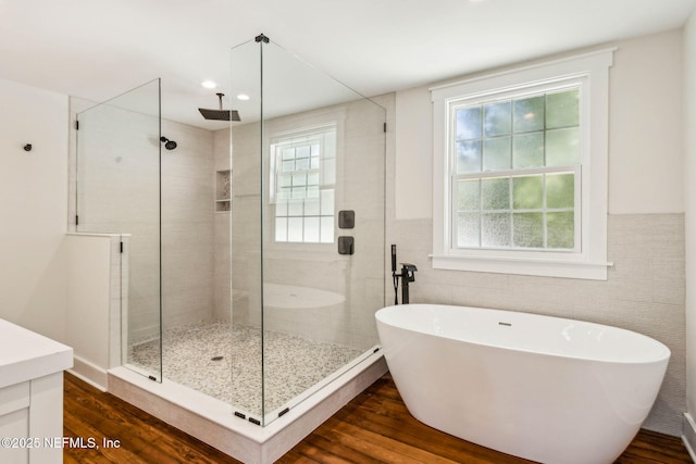 full bath with tile walls, a soaking tub, a stall shower, and wood finished floors