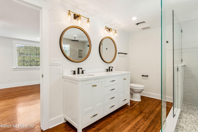 full bath featuring a tile shower, a sink, double vanity, toilet, and wood finished floors