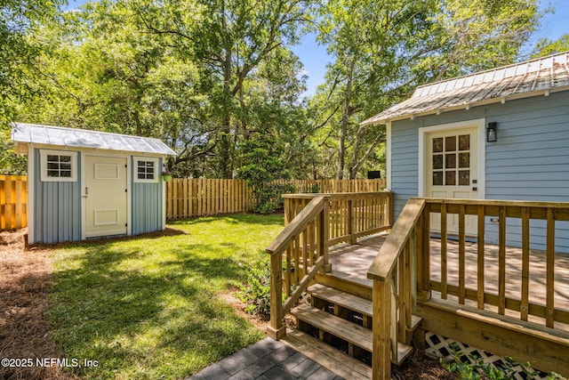 wooden terrace featuring a storage unit, a fenced backyard, an outbuilding, and a yard