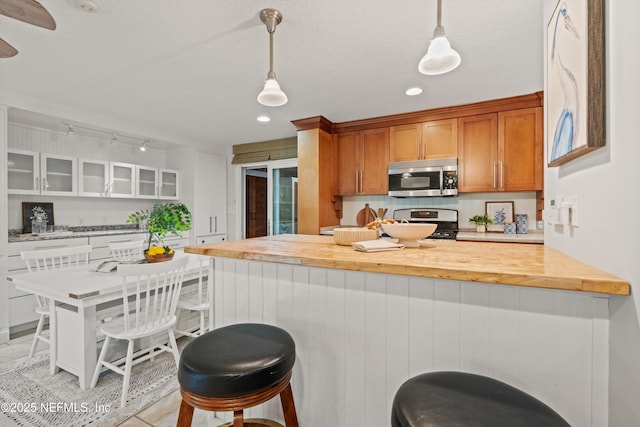 kitchen featuring stainless steel appliances, glass insert cabinets, a breakfast bar, brown cabinetry, and recessed lighting