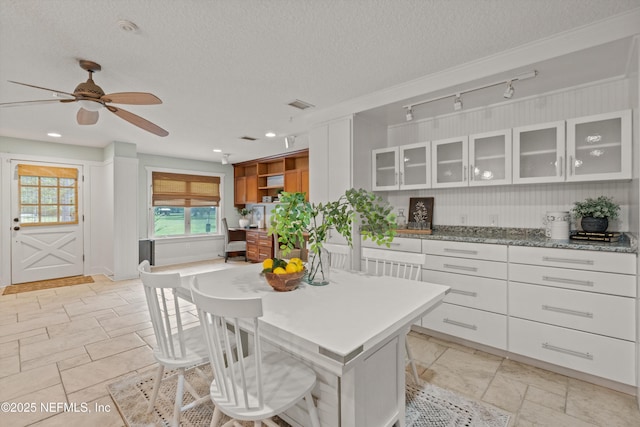 kitchen featuring a textured ceiling, white cabinetry, a ceiling fan, glass insert cabinets, and track lighting