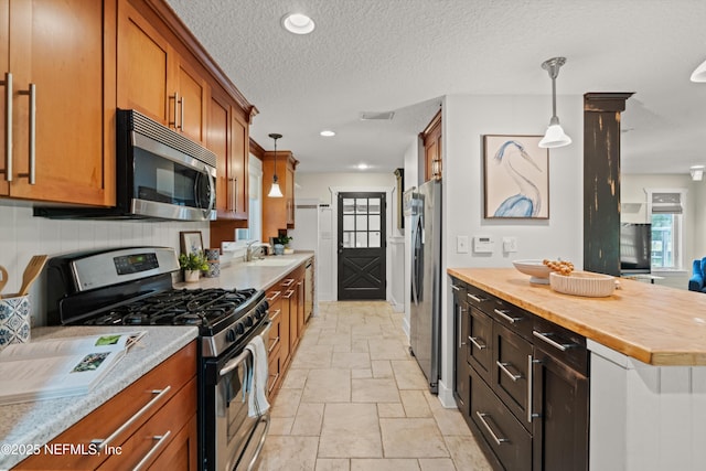 kitchen with appliances with stainless steel finishes, a sink, stone tile flooring, brown cabinets, and a textured ceiling