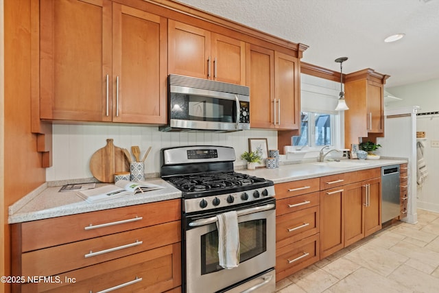 kitchen with appliances with stainless steel finishes, a sink, brown cabinets, decorative light fixtures, and light stone countertops