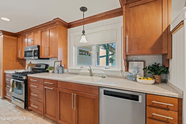 kitchen featuring stainless steel appliances, a sink, brown cabinetry, hanging light fixtures, and light stone counters
