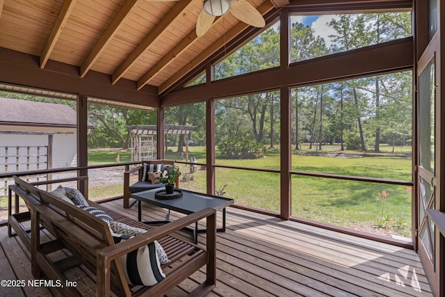 sunroom featuring a ceiling fan and view of wooded area