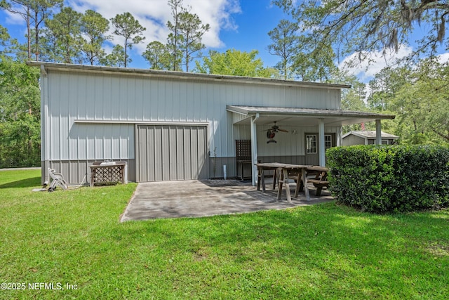 back of property with a ceiling fan, a lawn, an outdoor structure, and a pole building