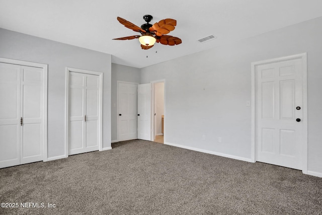 unfurnished bedroom with baseboards, carpet, visible vents, and two closets