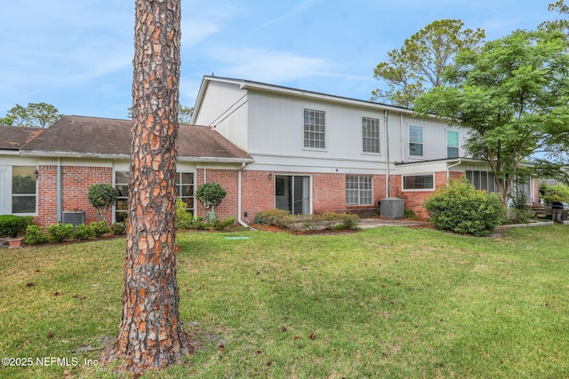 back of property featuring brick siding, a yard, and central AC