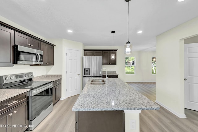 kitchen with dark brown cabinets, light wood-style flooring, appliances with stainless steel finishes, and an island with sink