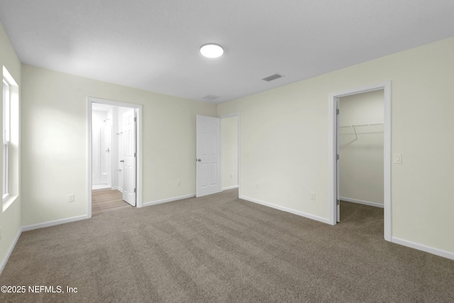 unfurnished bedroom featuring a spacious closet, baseboards, visible vents, and carpet