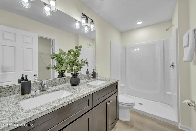 bathroom featuring toilet, wood finished floors, a sink, and a stall shower