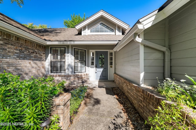 view of exterior entry with a shingled roof and brick siding