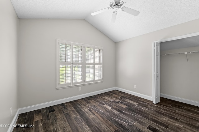 unfurnished bedroom with dark wood finished floors, vaulted ceiling, baseboards, a ceiling fan, and a closet