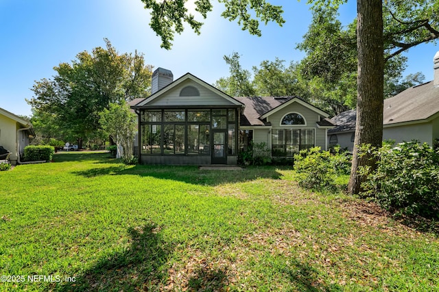 back of property featuring a sunroom, a chimney, roof with shingles, and a lawn