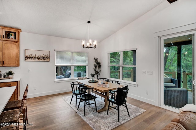 dining space with baseboards, a wealth of natural light, lofted ceiling, and an inviting chandelier