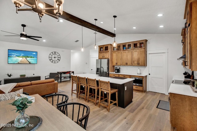 kitchen featuring light wood-style flooring, open floor plan, vaulted ceiling with beams, stainless steel fridge with ice dispenser, and brown cabinetry