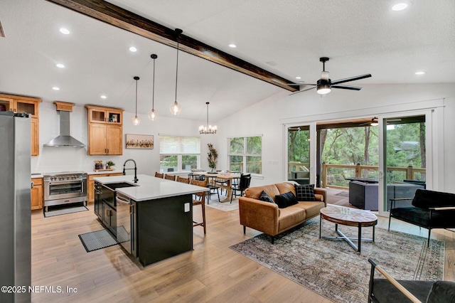 kitchen with light countertops, vaulted ceiling with beams, wall chimney exhaust hood, appliances with stainless steel finishes, and ceiling fan with notable chandelier
