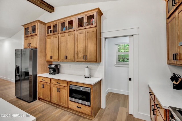 kitchen with light wood finished floors, oven, light countertops, vaulted ceiling with beams, and black fridge with ice dispenser