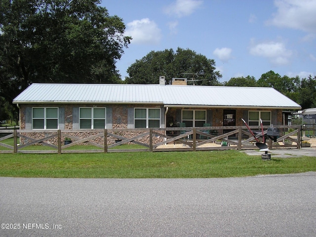 view of front of house featuring a front yard, stone siding, a chimney, and metal roof