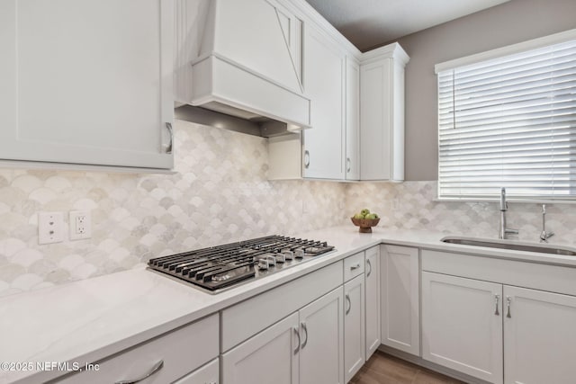 kitchen with custom exhaust hood, a sink, stainless steel gas stovetop, and light countertops