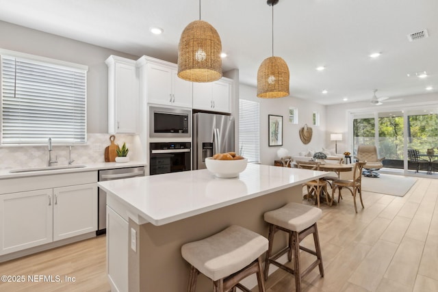 kitchen featuring stainless steel appliances, light countertops, visible vents, a sink, and open floor plan