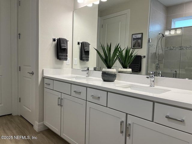 bathroom with double vanity, wood finished floors, a stall shower, and a sink