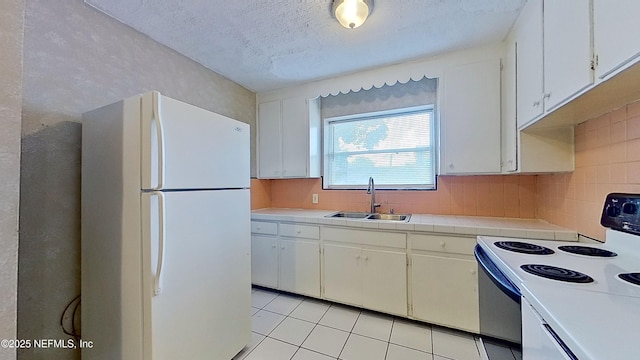 kitchen with light tile patterned floors, a sink, freestanding refrigerator, decorative backsplash, and electric range oven