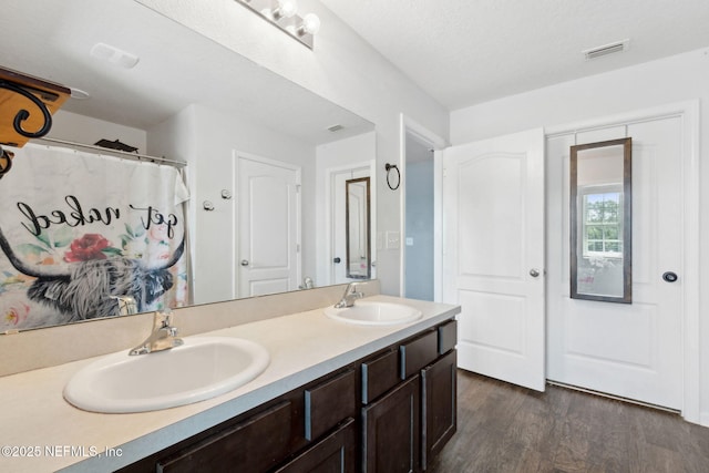 full bathroom with double vanity, wood finished floors, visible vents, and a sink