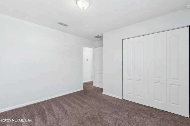 unfurnished bedroom with dark carpet, baseboards, visible vents, and a closet