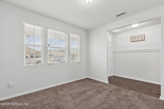 spare room with dark colored carpet, visible vents, and baseboards