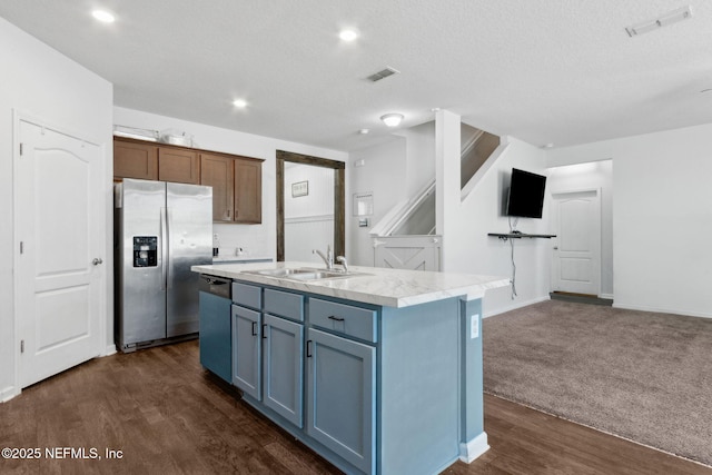 kitchen with an island with sink, light countertops, dishwasher, a sink, and stainless steel fridge