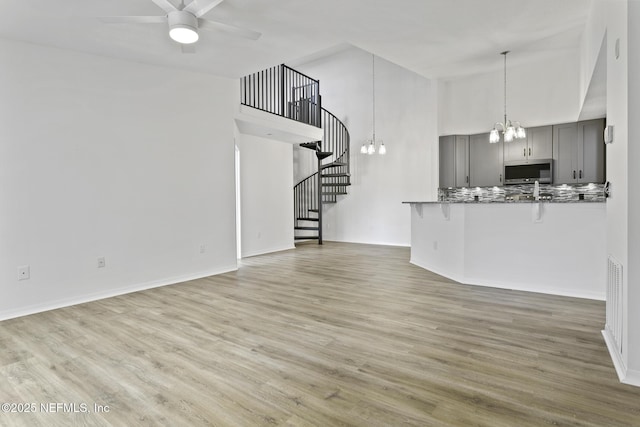 11213 Harbour Vista Cir, Saint Augustine, FL 32080 - kitchen featuring gray cabinets, stainless steel microwave, ceiling fan with notable chandelier, a high ceiling, and a breakfast bar