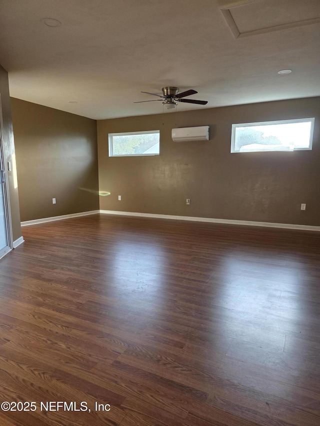 unfurnished room with a wall mounted air conditioner, ceiling fan, baseboards, and dark wood finished floors