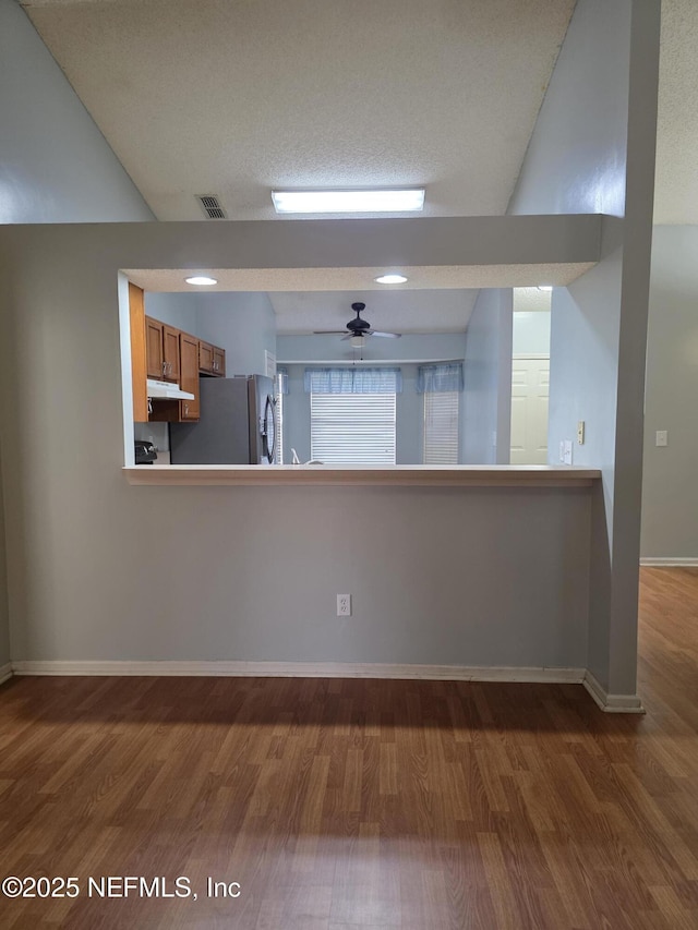 kitchen featuring visible vents, freestanding refrigerator, under cabinet range hood, wood finished floors, and brown cabinetry