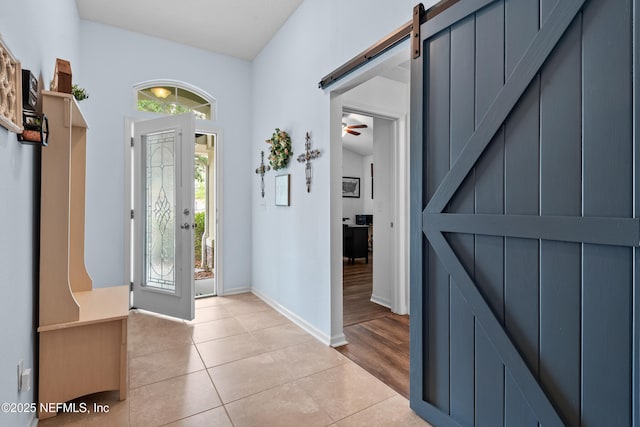 entryway featuring baseboards, ceiling fan, a barn door, and light tile patterned floors