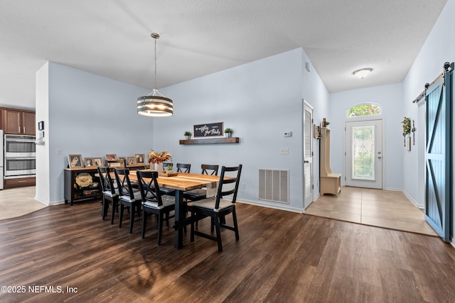 dining area with a notable chandelier, a barn door, baseboards, wood finished floors, and visible vents