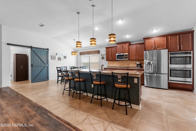 kitchen featuring stainless steel appliances, a barn door, a kitchen breakfast bar, and a center island with sink