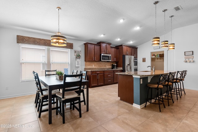 kitchen with backsplash, a kitchen bar, visible vents, appliances with stainless steel finishes, and a sink