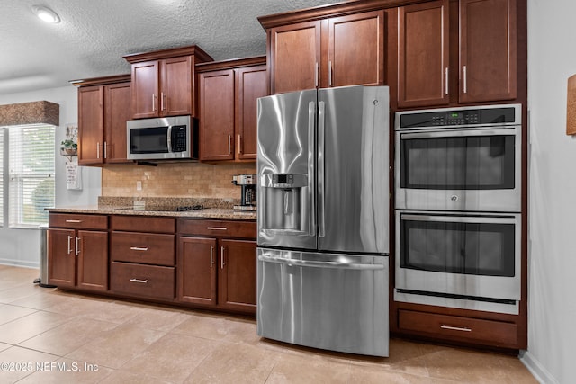 kitchen with stone countertops, baseboards, a textured ceiling, tasteful backsplash, and appliances with stainless steel finishes
