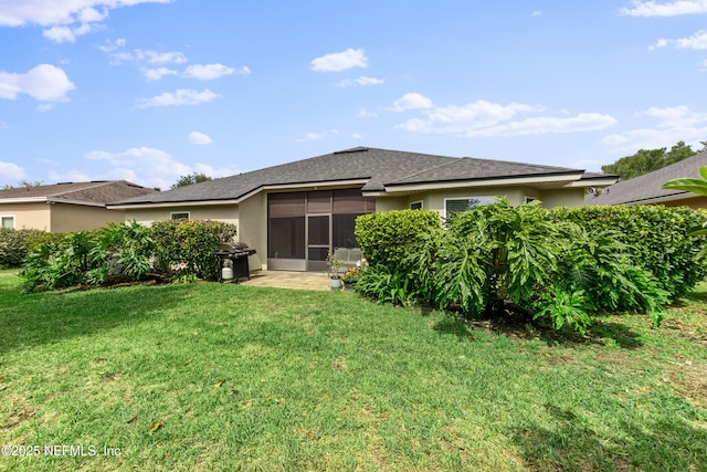 back of house featuring a sunroom, roof with shingles, stucco siding, and a yard
