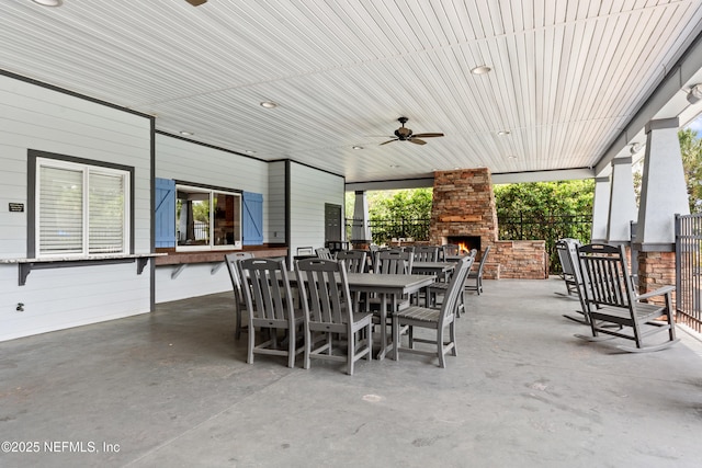 view of patio / terrace featuring outdoor dining area, a ceiling fan, a large fireplace, and fence