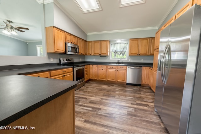 kitchen with a sink, dark wood-style flooring, dark countertops, crown molding, and appliances with stainless steel finishes
