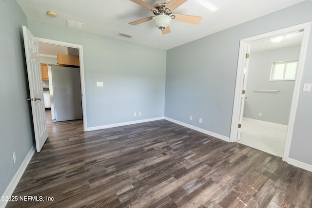 spare room featuring dark wood-type flooring, visible vents, a ceiling fan, and baseboards