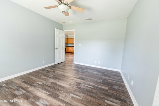 unfurnished room with dark wood-type flooring, visible vents, a ceiling fan, and baseboards